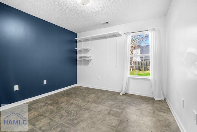 unfurnished room with baseboards, visible vents, and a textured ceiling