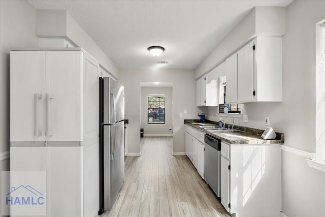 kitchen with sink, light hardwood / wood-style flooring, a textured ceiling, appliances with stainless steel finishes, and white cabinetry