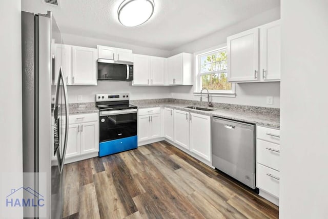 kitchen with light stone counters, stainless steel appliances, sink, dark hardwood / wood-style floors, and white cabinetry