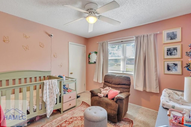 carpeted bedroom featuring ceiling fan, a nursery area, and a textured ceiling