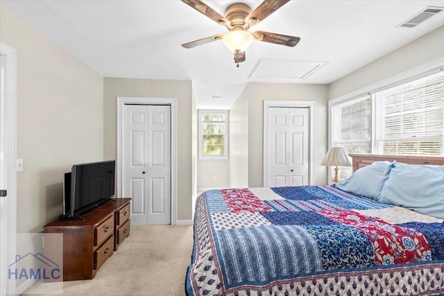 bedroom featuring two closets, multiple windows, light colored carpet, and ceiling fan