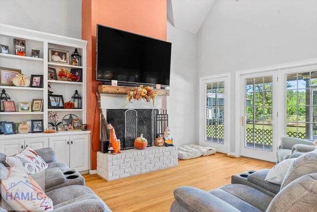 living room featuring high vaulted ceiling, light hardwood / wood-style floors, and a brick fireplace