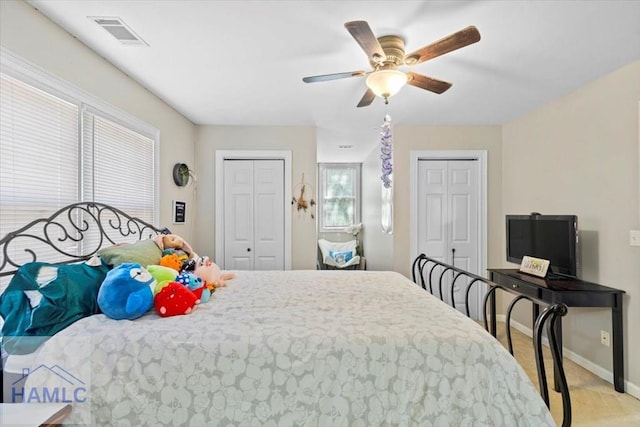 bedroom featuring multiple closets, ceiling fan, and light carpet