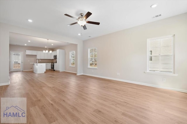 unfurnished living room with ceiling fan with notable chandelier, sink, and light hardwood / wood-style floors