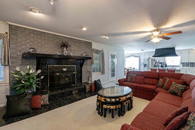 living room featuring a brick fireplace, crown molding, a textured ceiling, and ceiling fan