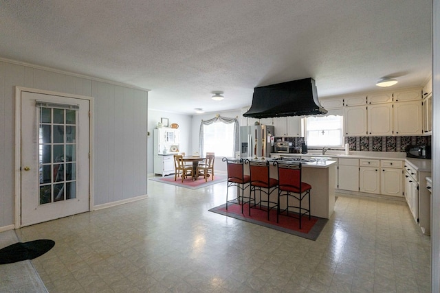 kitchen with stainless steel refrigerator with ice dispenser, a kitchen island, a wealth of natural light, and a kitchen bar