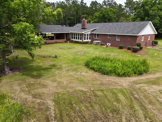 back of house featuring a sunroom, central AC unit, and a lawn