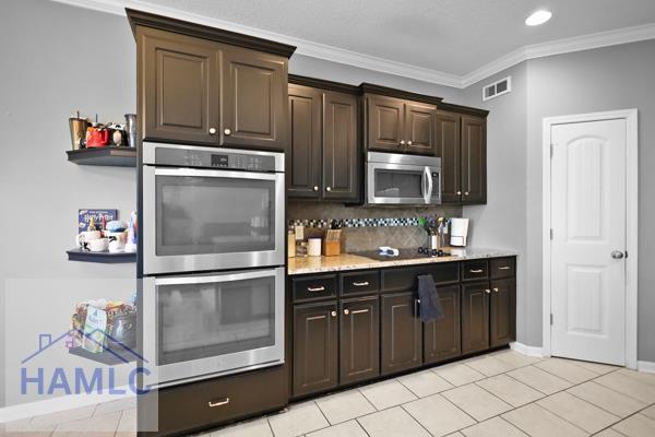 246 Cumberland Dr NE, Ludowici, GA 31316 - kitchen with stainless steel appliances, decorative backsplash, crown molding, dark brown cabinetry, and light tile patterned floors