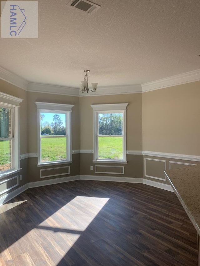 unfurnished dining area with wood finished floors, a textured ceiling, an inviting chandelier, ornamental molding, and visible vents