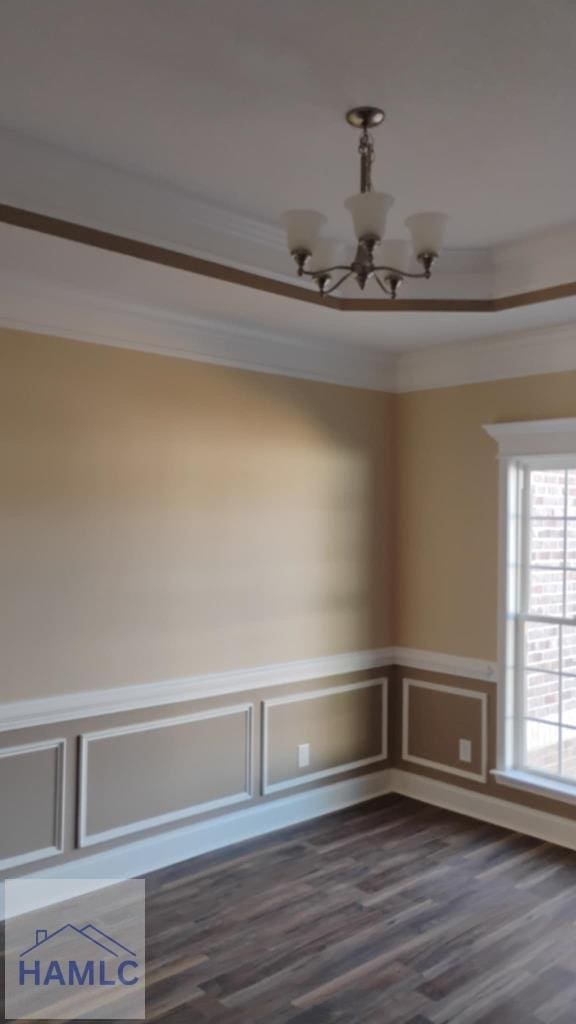empty room featuring wainscoting, a notable chandelier, crown molding, and dark wood-style floors