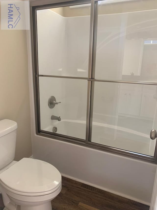 bathroom featuring toilet, bath / shower combo with glass door, and wood finished floors