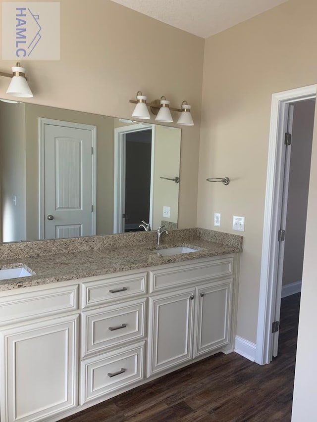 full bathroom featuring double vanity, baseboards, wood finished floors, and a sink