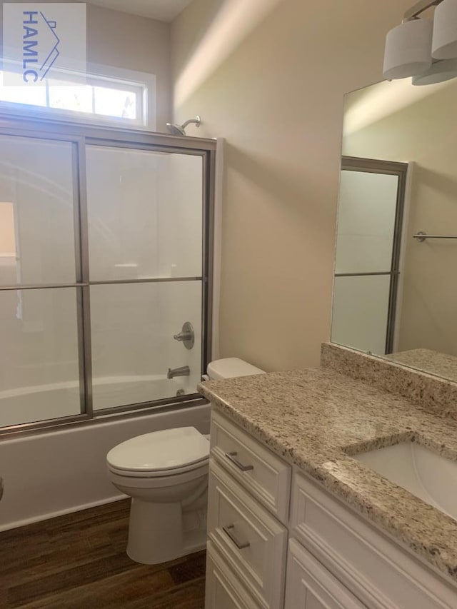 bathroom with enclosed tub / shower combo, toilet, vanity, and wood finished floors