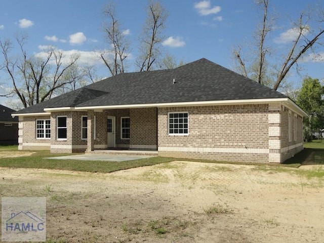 rear view of property with brick siding, a patio area, and a shingled roof