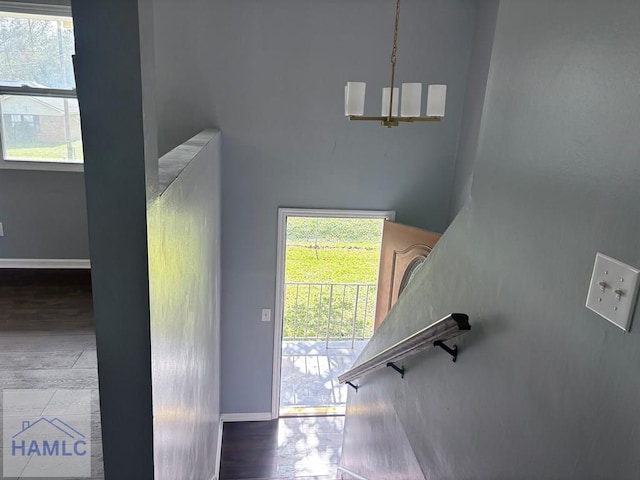 stairs with a chandelier, baseboards, a healthy amount of sunlight, and wood finished floors