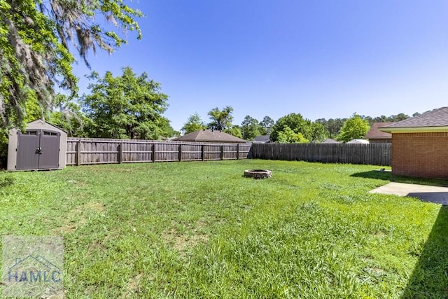 view of yard featuring a storage shed, a fenced backyard, an outdoor structure, and an outdoor fire pit