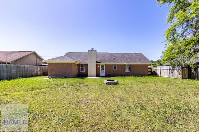 back of property featuring a yard, brick siding, a fenced backyard, and an outdoor fire pit