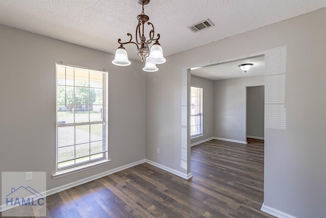 empty room with a chandelier, visible vents, a wealth of natural light, and wood finished floors