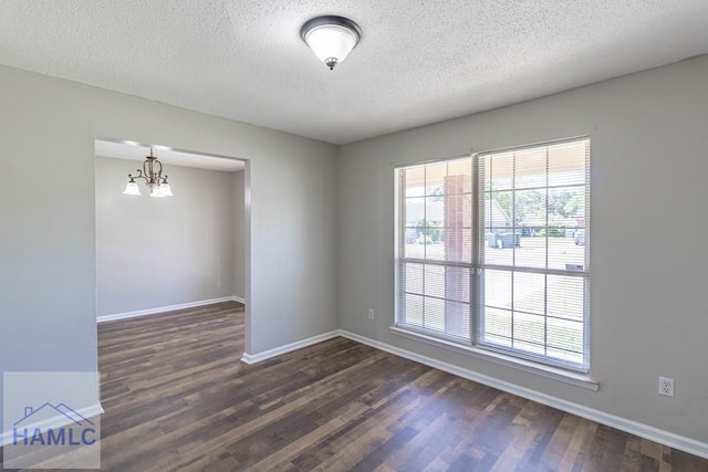 spare room with dark wood-style floors, a notable chandelier, and a wealth of natural light