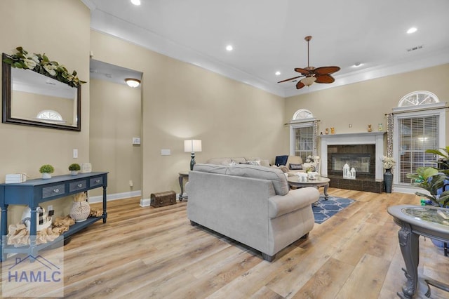 living room featuring a fireplace, light hardwood / wood-style floors, ceiling fan, and crown molding