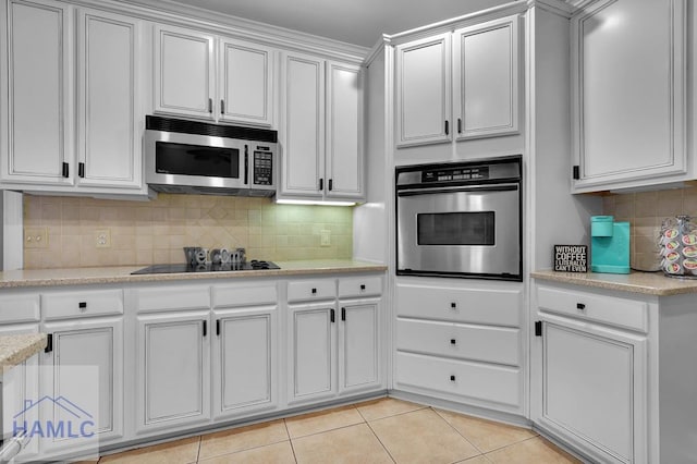 kitchen with appliances with stainless steel finishes, backsplash, white cabinetry, light tile patterned floors, and light stone counters