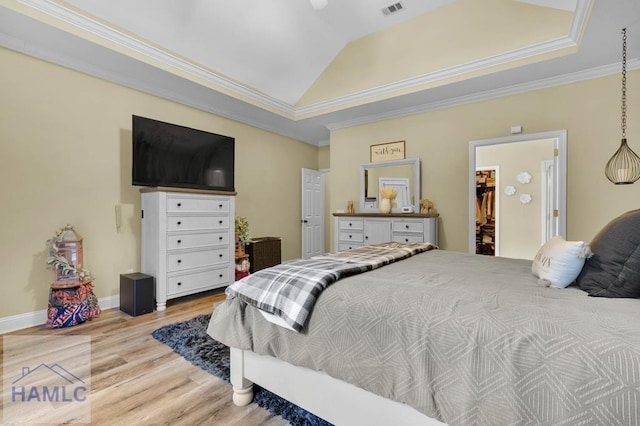 bedroom featuring a spacious closet, light hardwood / wood-style floors, a closet, ornamental molding, and vaulted ceiling