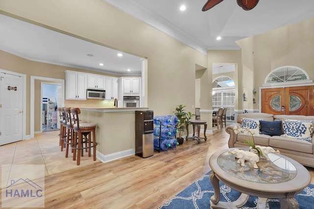 living room with light hardwood / wood-style floors, ornamental molding, and ceiling fan