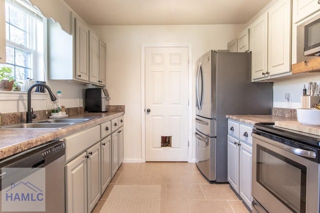 kitchen with white cabinets, appliances with stainless steel finishes, light countertops, a sink, and light tile patterned flooring