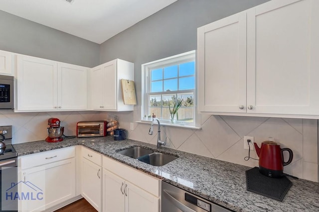 kitchen with white cabinetry, tasteful backsplash, a sink, stone counters, and stainless steel appliances