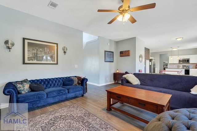living area featuring baseboards, ceiling fan, wood finished floors, and visible vents