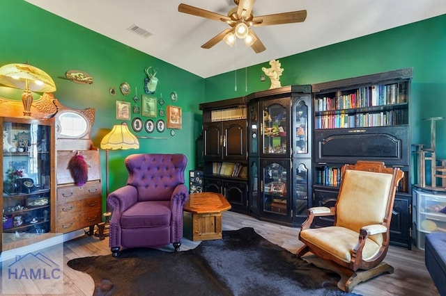 living area with a ceiling fan, vaulted ceiling, wood finished floors, and visible vents