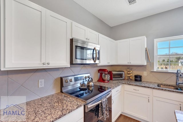 kitchen with a sink, appliances with stainless steel finishes, white cabinets, and light stone counters