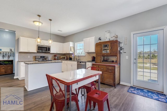 kitchen featuring decorative backsplash, a kitchen island, appliances with stainless steel finishes, wood finished floors, and a sink