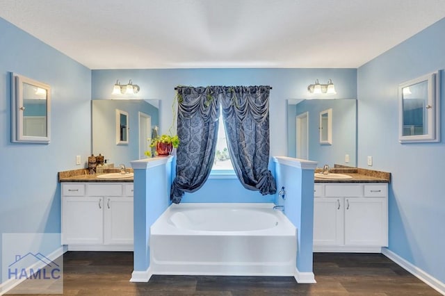 full bathroom with a sink, two vanities, wood finished floors, and a garden tub