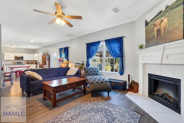 living area featuring a fireplace, a ceiling fan, light wood finished floors, and visible vents