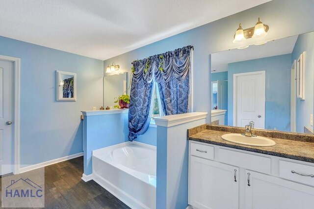 full bath featuring vanity, baseboards, a garden tub, and wood finished floors