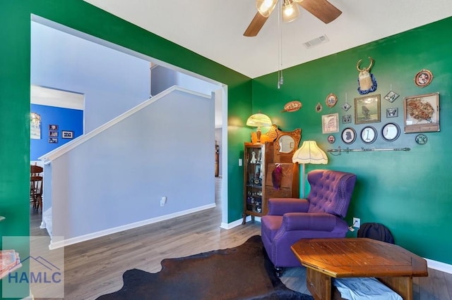 sitting room with visible vents, stairs, wood finished floors, baseboards, and a ceiling fan