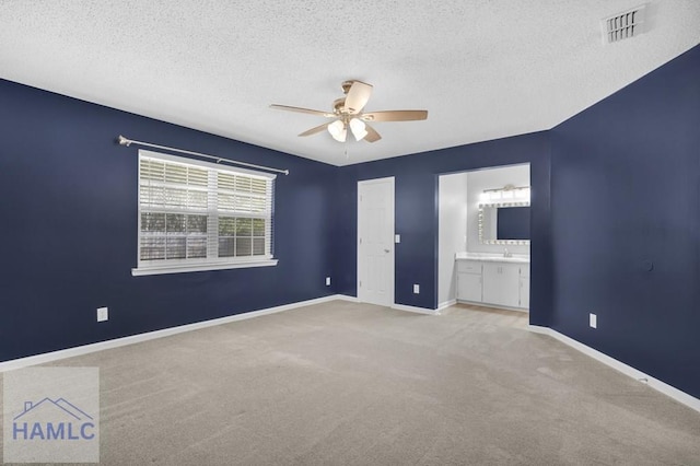 unfurnished bedroom with a textured ceiling, connected bathroom, ceiling fan, sink, and light colored carpet