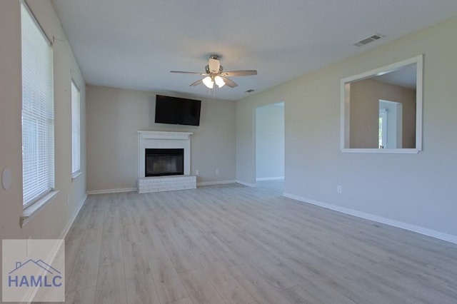unfurnished living room featuring ceiling fan, light wood finished floors, a fireplace, baseboards, and visible vents