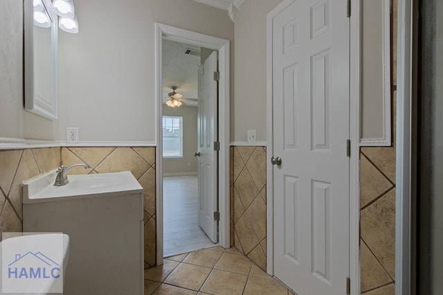 bathroom with tile walls, vanity, ceiling fan, a wainscoted wall, and tile patterned flooring
