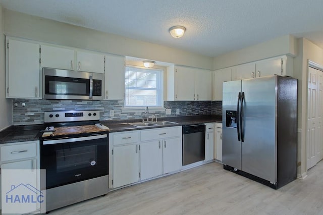 kitchen featuring light wood finished floors, a sink, backsplash, dark countertops, and appliances with stainless steel finishes