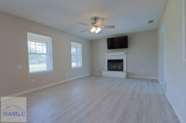 unfurnished living room with ceiling fan, light wood finished floors, a fireplace, baseboards, and visible vents