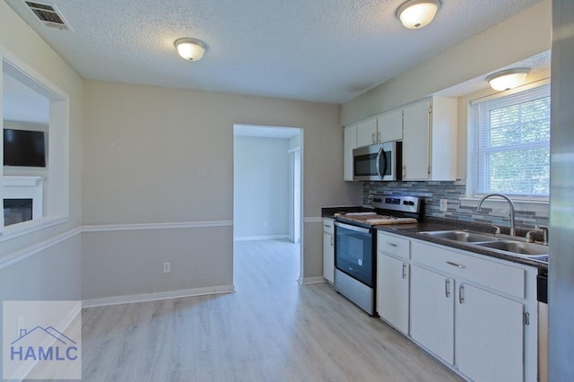 kitchen with stainless steel microwave, electric stove, a sink, decorative backsplash, and white cabinets