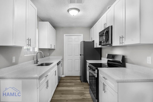 905 Greenbriar Rd, Hinesville, GA 31313 - kitchen featuring appliances with stainless steel finishes, a sink, wood finished floors, white cabinetry, and a textured ceiling