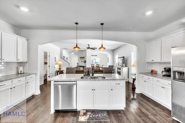 kitchen with stainless steel appliances, a sink, arched walkways, ceiling fan, and a kitchen island with sink