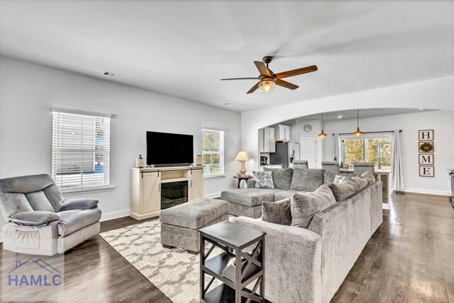 living area with visible vents, plenty of natural light, ceiling fan, arched walkways, and dark wood-type flooring