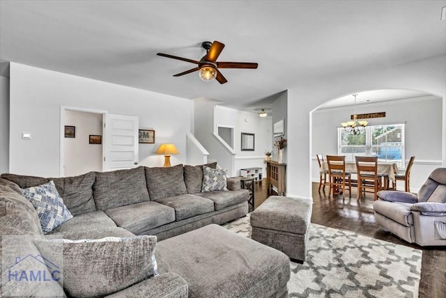 living area featuring baseboards, ornamental molding, wood finished floors, arched walkways, and ceiling fan with notable chandelier