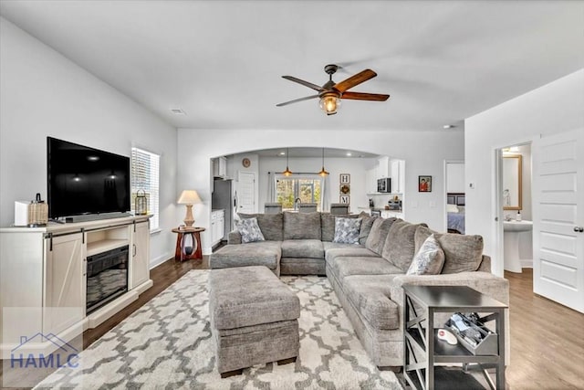 living room featuring arched walkways, ceiling fan, wood finished floors, and a healthy amount of sunlight