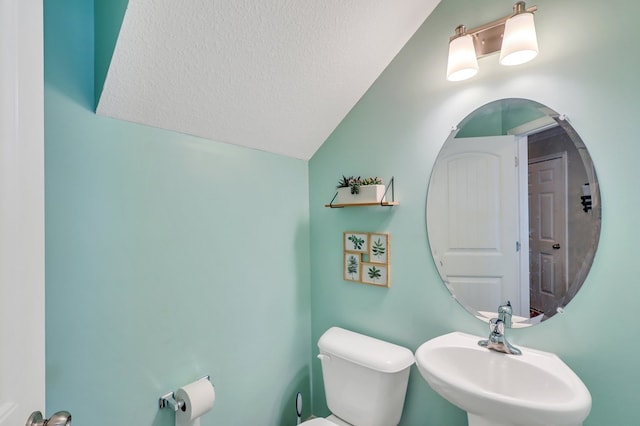 bathroom with a textured ceiling, toilet, lofted ceiling, and sink