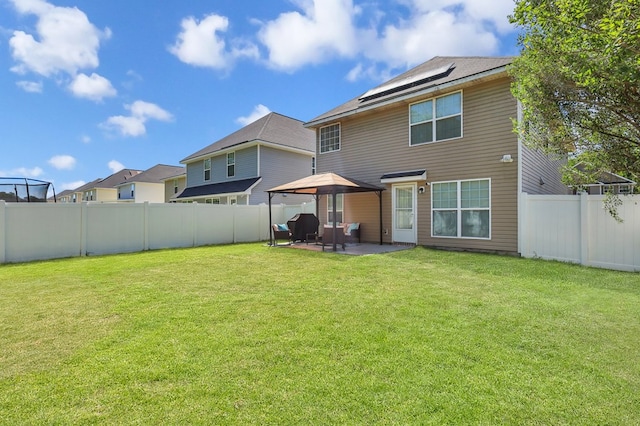 rear view of property featuring a gazebo, a patio area, a yard, and solar panels